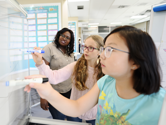 Students solving math problems on a whiteboard with their educator